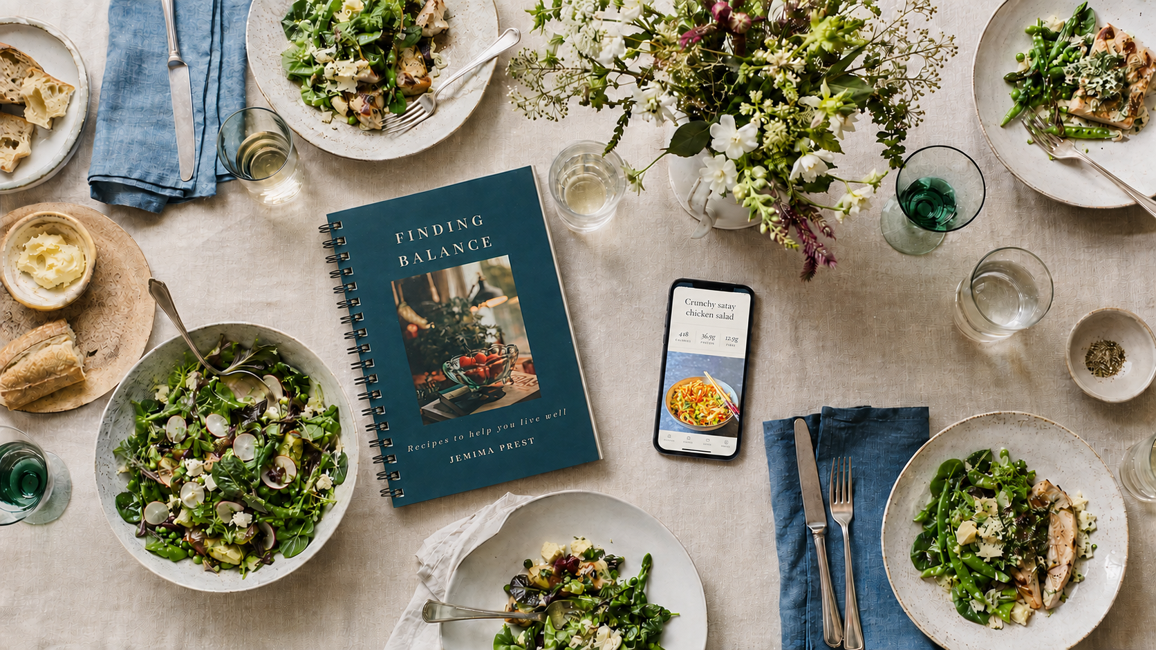 An overhead view of a relaxed table laid with food, flowers, the Finding Balance book and a phone showing the app